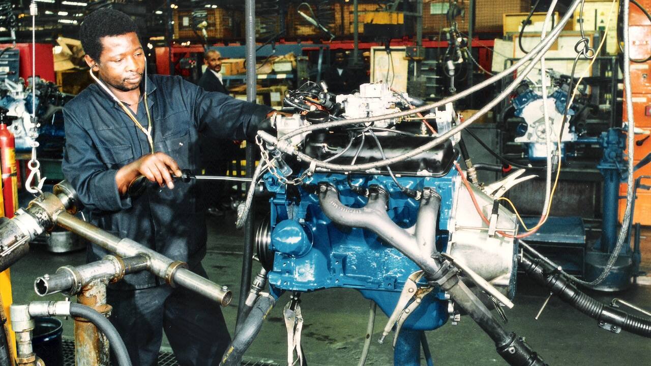 A worker handles the Essex V6 engine on the assembly line