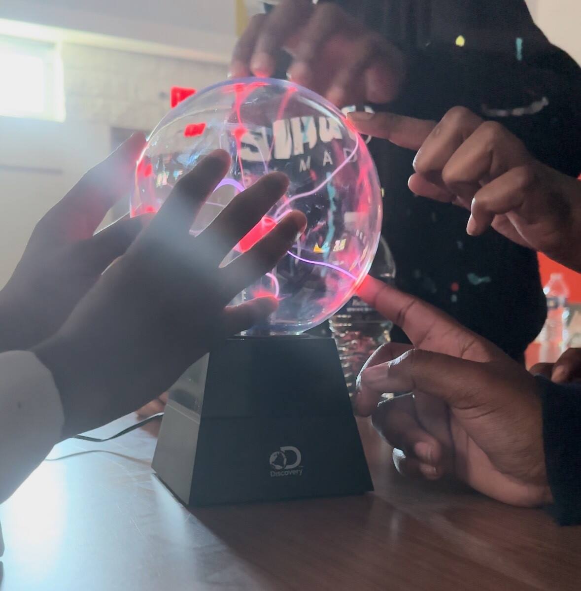 Children's hands touch a plasma ball lamp.