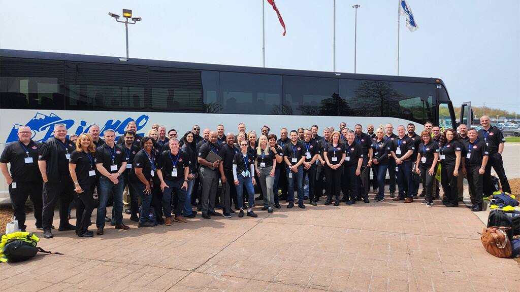 Ford employees stand in one large group in front of the tour bus.