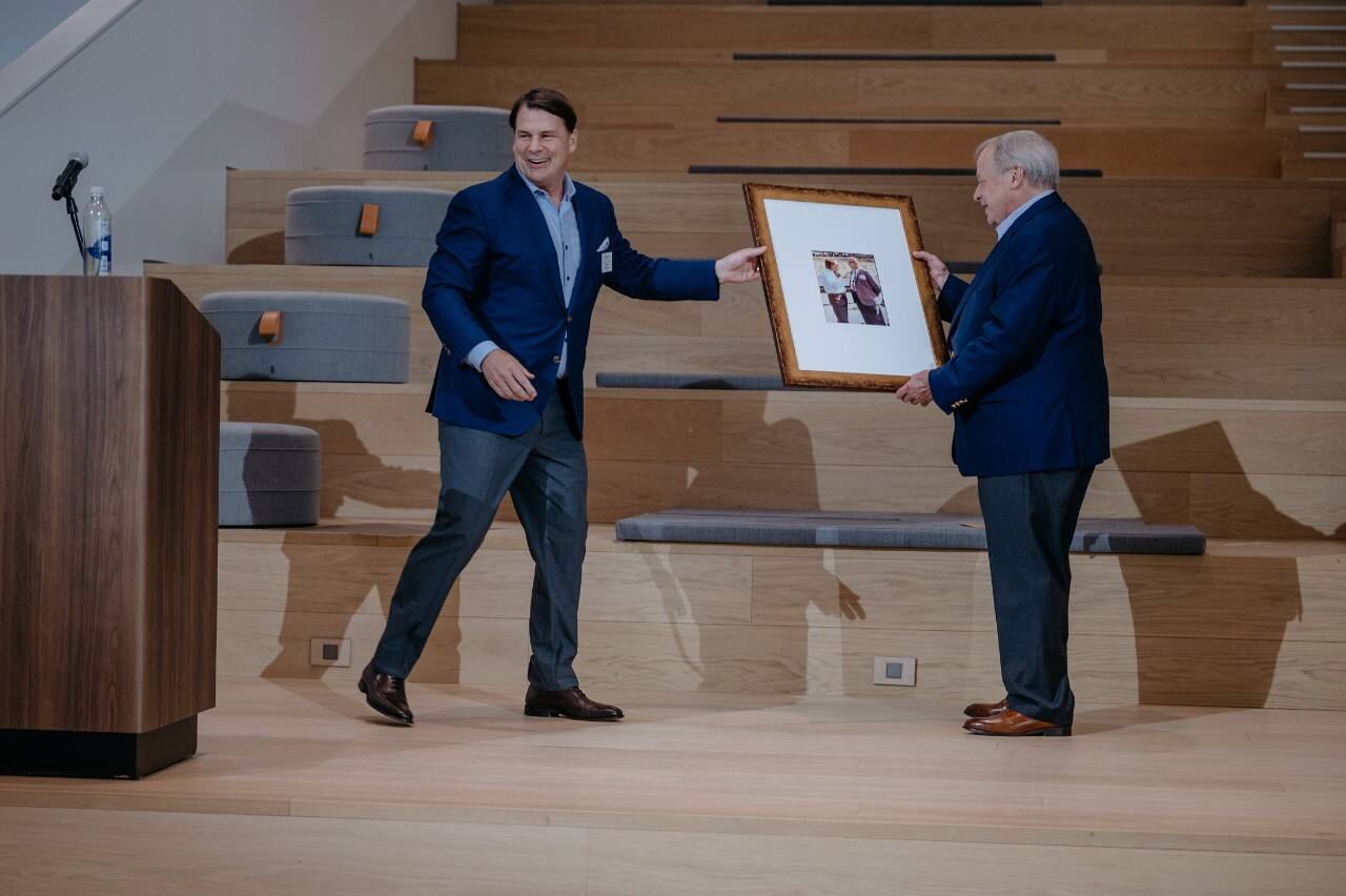   Ford President and CEO Jim Farley presents Edsel Ford II with a framed photo of the late Ford racing legend John Holman.
