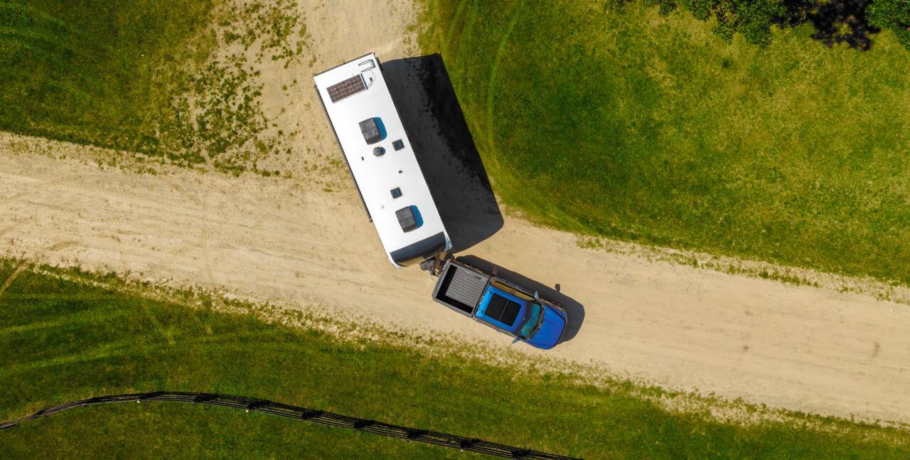 Viewed from the top, F-150 turns on a dirt road, towing a large trailer.