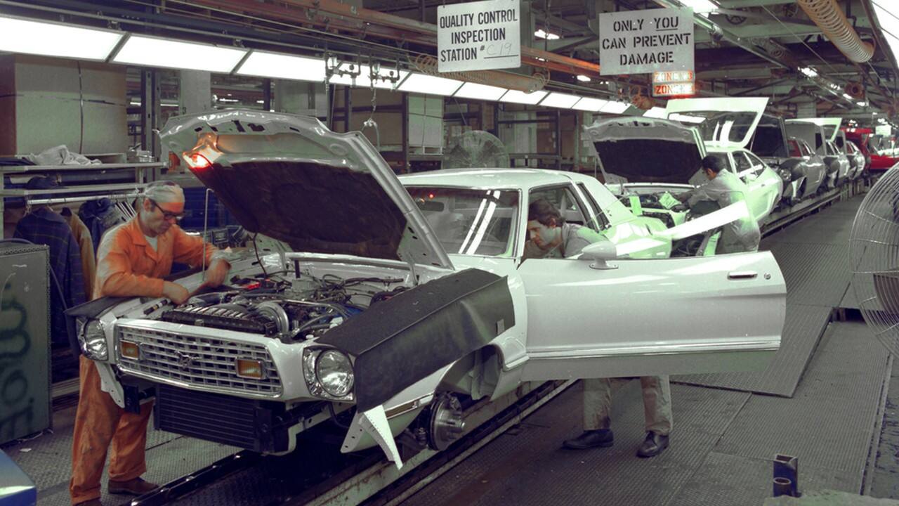 A worker handles the Mustang II engine on the assembly line