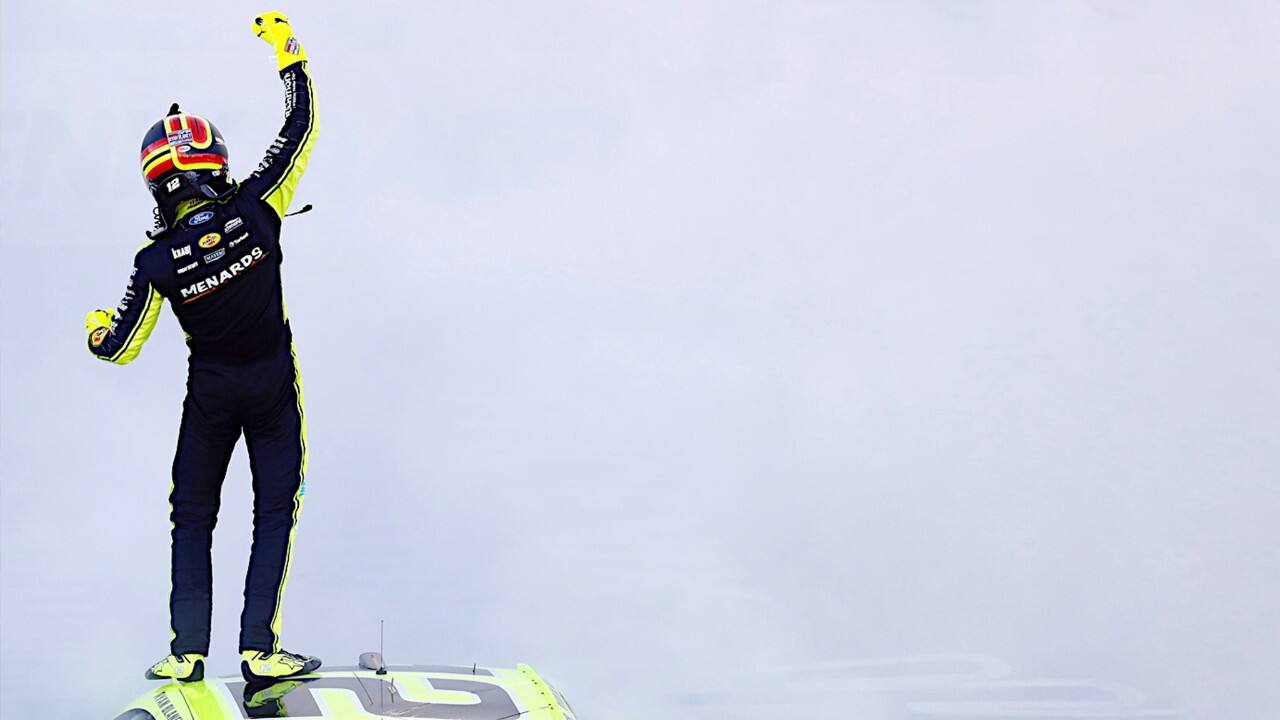 Ryan Blaney stands on top of his racecar amid the smoke