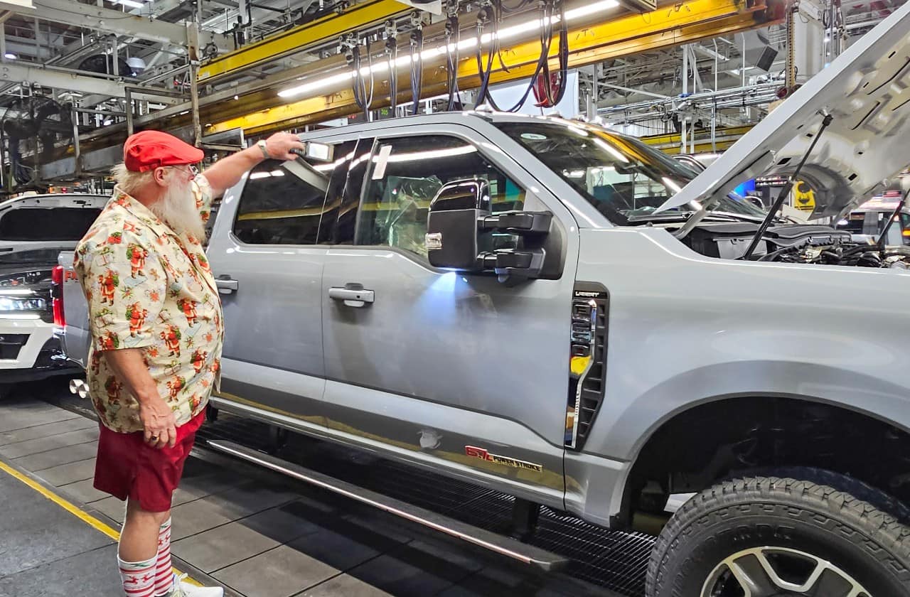 Larry works on a truck on the assembly line while wearing a Christmas-themed outfit
